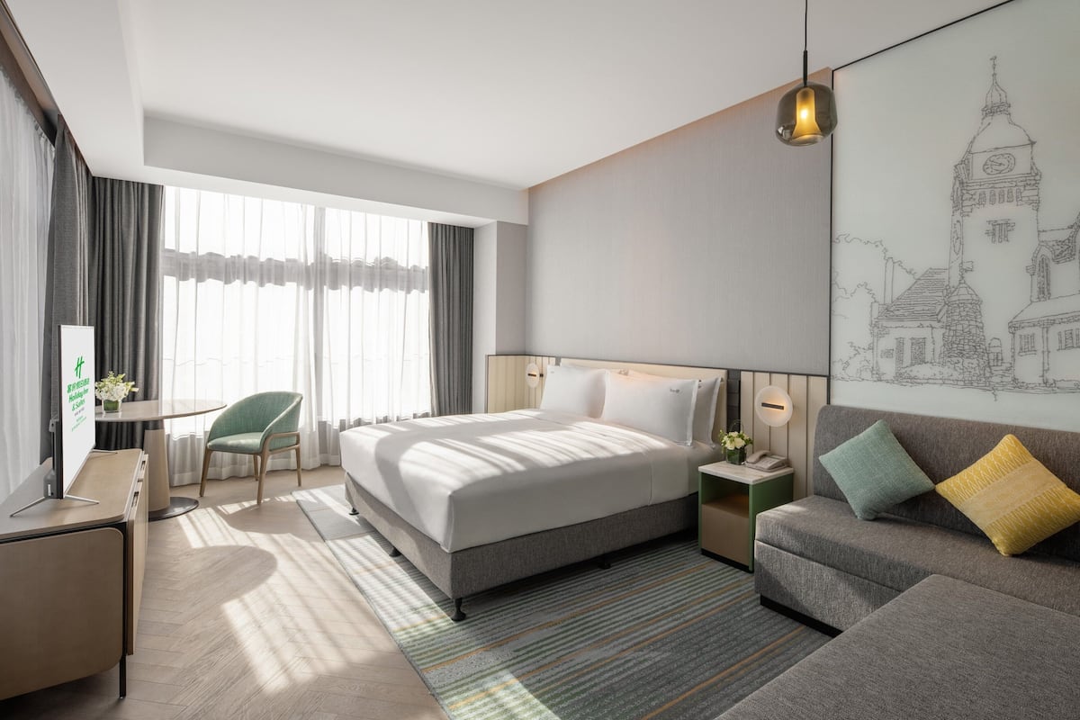 A modern hotel room with a large bed, a sofa, a desk, and a chair.
