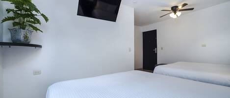 Una camera d'albergo con due letti, una ventola a soffitto, una TV a schermo piatto e una pianta in vaso.