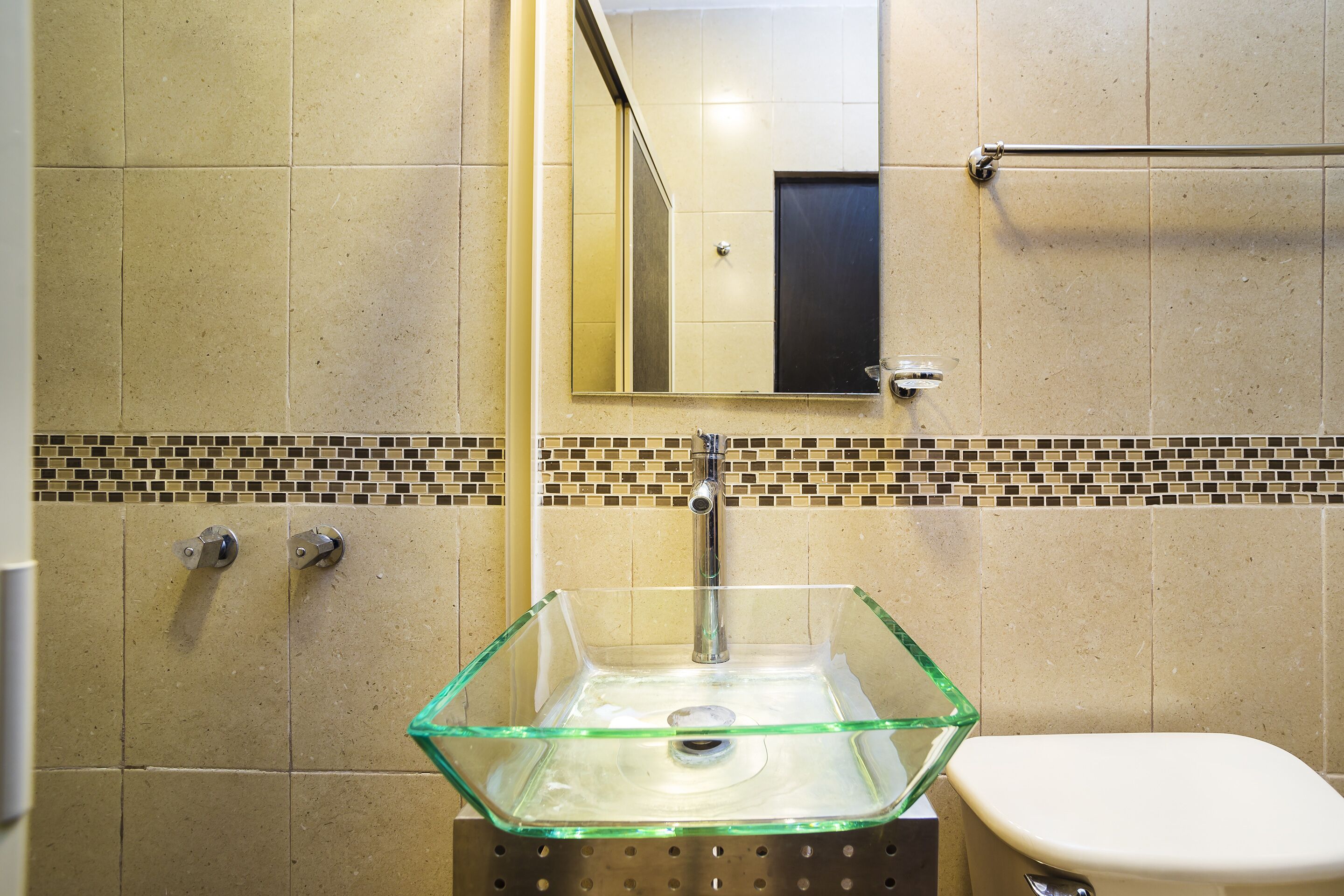 Une salle de bain avec un lavabo en verre, des toilettes et un miroir.
