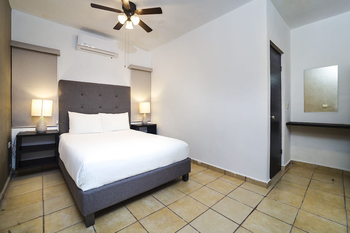 Une chambre d’hôtel équipée d’un lit, de deux lampes de chevet, d’un ventilateur de plafond et d’un climatiseur fixé au mur.