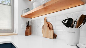 Eine Küche mit weißen Arbeitsplatten, Holzböden und einem Utensilienhalter mit der Aufschrift 'UTENSILS'.