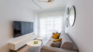 Moderni olohuone, jossa on litteänäyttöinen televisio, koristetyynyillä varustettu sohva, pieni pöytä ja kattotuuletin.