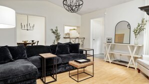 Un salon moderne comprenant un canapé d’angle, une table basse, une table d’appoint, un luminaire suspendu et une console avec un miroir.