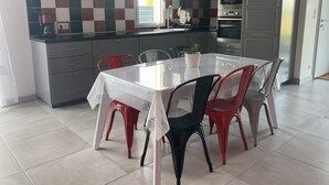 Una cocina moderna con armarios grises, un salpicadero a cuadros y una zona de comedor con mesa blanca y sillas rojas.