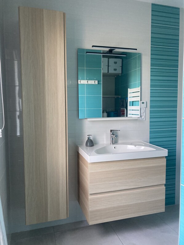 A modern bathroom with a wooden vanity, a white sink, and a mirror with a teal backsplash. - 4* gite close to Puy du Fou open all year round (Chavagnes-en-Paillers)