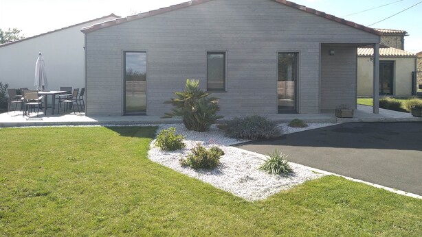 Una casa moderna de dos pisos con techo plano, ventanas amplias y un patio con mobiliario exterior.