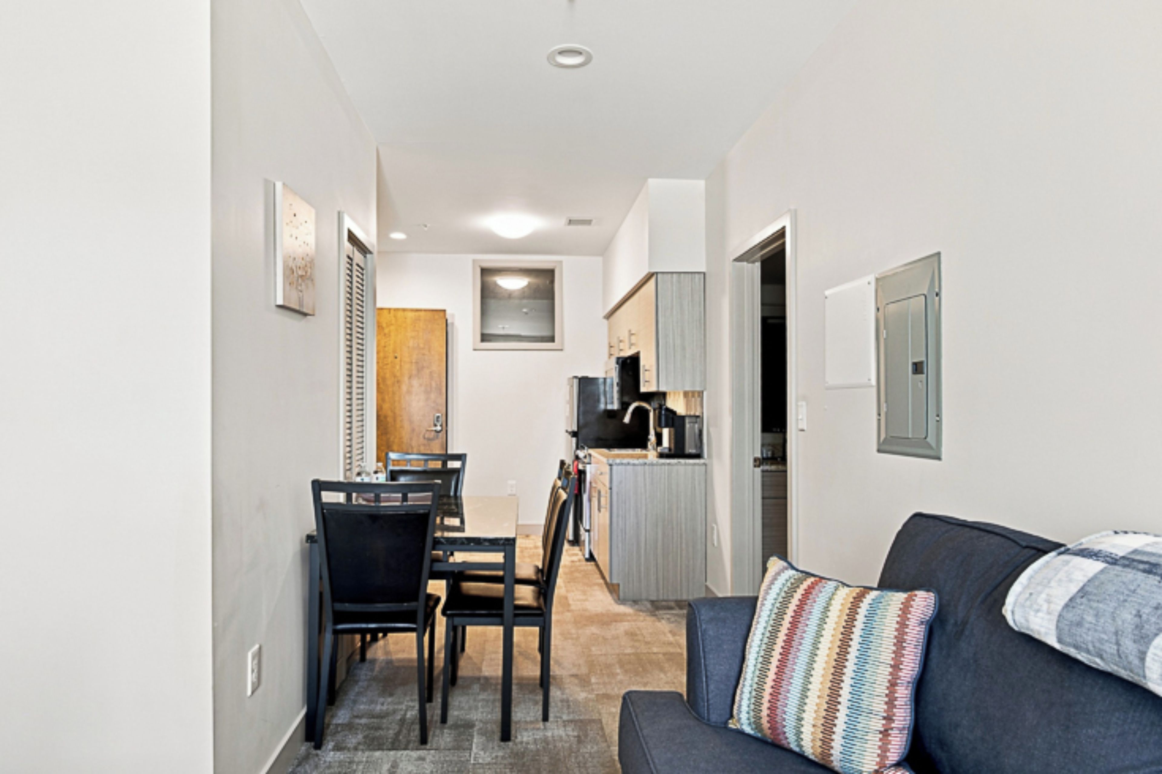 A compact living space with a dining area, kitchenette, and a sofa with a colorful pillow.