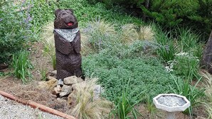 A garden with a bear statue, a bird bath, and various plants.