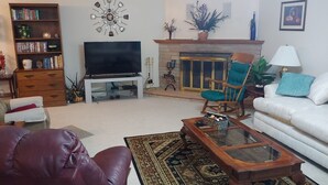 A living room with a television, a fireplace, a sofa, a rocking chair, and a bookshelf.