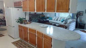 A kitchen with wooden cabinets, a refrigerator, and a dining area with a sofa and a lamp.