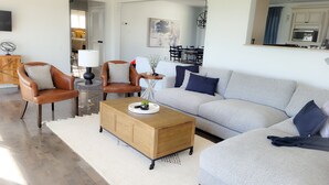 A modern living room with a grey sofa, two brown leather armchairs, a wooden coffee table, and a white rug.