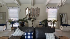 Een woonkamer met een zwarte leren bank, een houten salontafel en twee bijzettafeltjes. Er staan potplanten en er hangt een spiegel aan de muur.