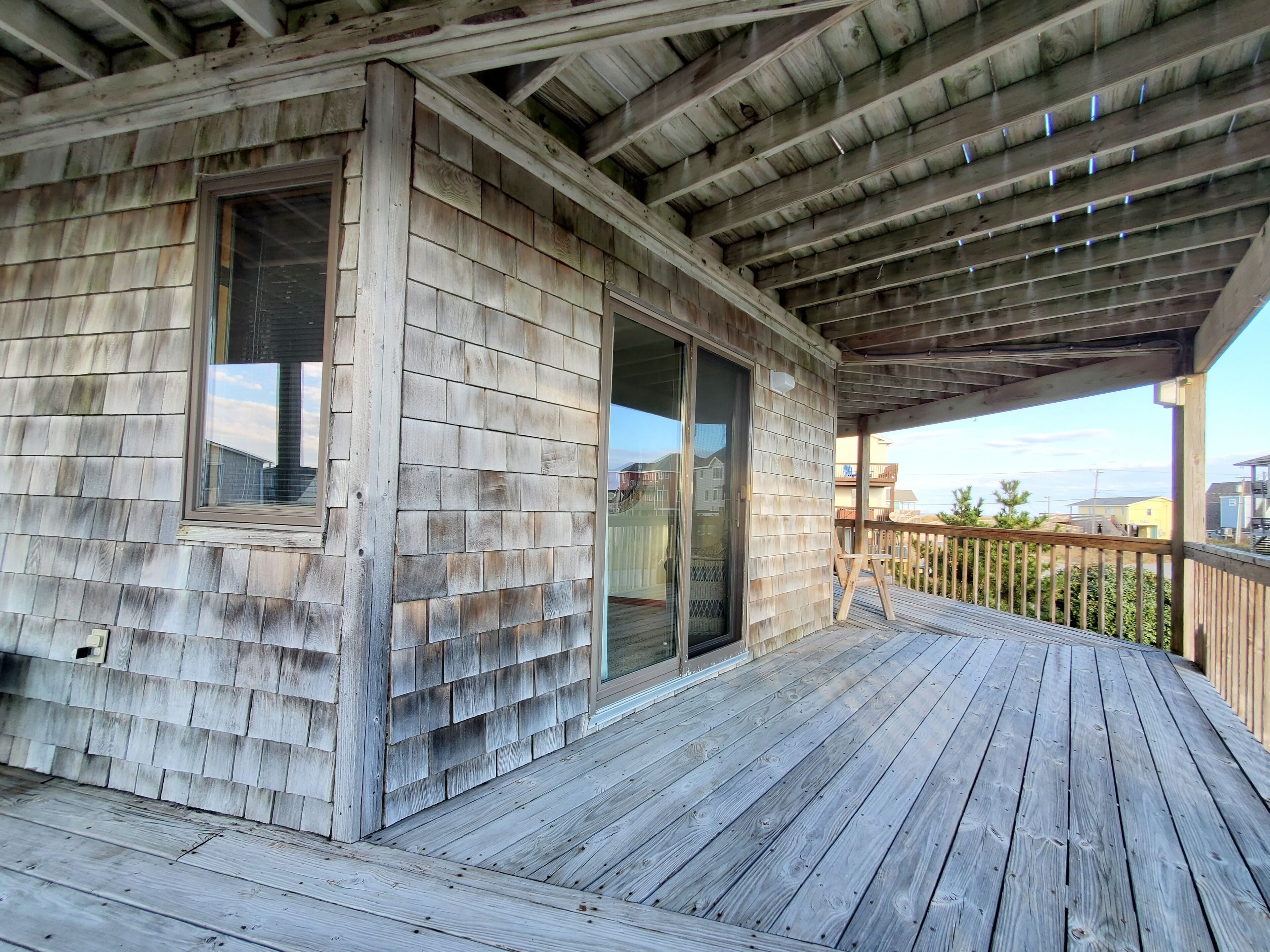 A wooden deck with a covered area, large sliding glass doors, and a view of the ocean.