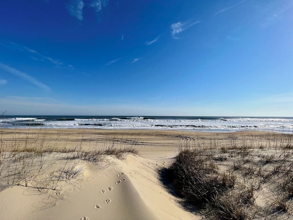 A beach with footprints in the sand and waves crashing onto the shore.