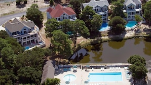 An aerial view of a residential area with multiple houses, a swimming pool, and a small lake. - Corolla Light Resort! Dogs! Heated Pool! Hot tub! Walk to restaurants! C1131 (Corolla)