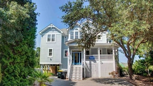 A two-story house with a porch and a blue door, surrounded by trees and a small garden. - Corolla Light Resort! Dogs! Heated Pool! Hot tub! Walk to restaurants! C1131 (Corolla)