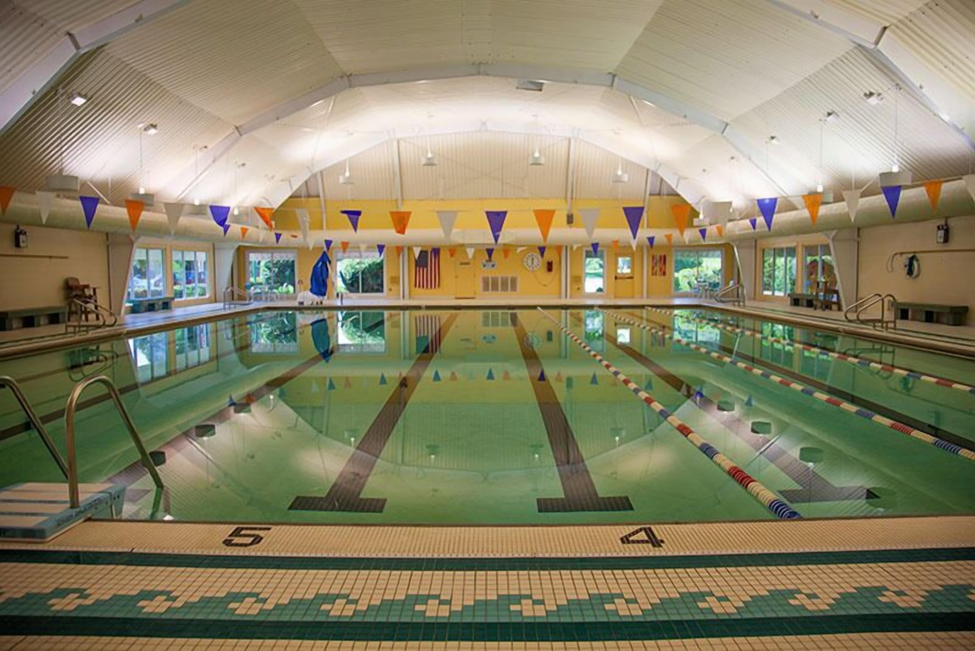 An indoor swimming pool with lanes, a tiled floor, and a high ceiling with triangular decorations.