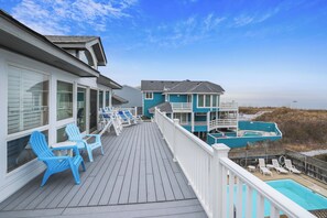 Um deck de madeira com cadeiras Adirondack azuis, uma piscina e vista para a praia.