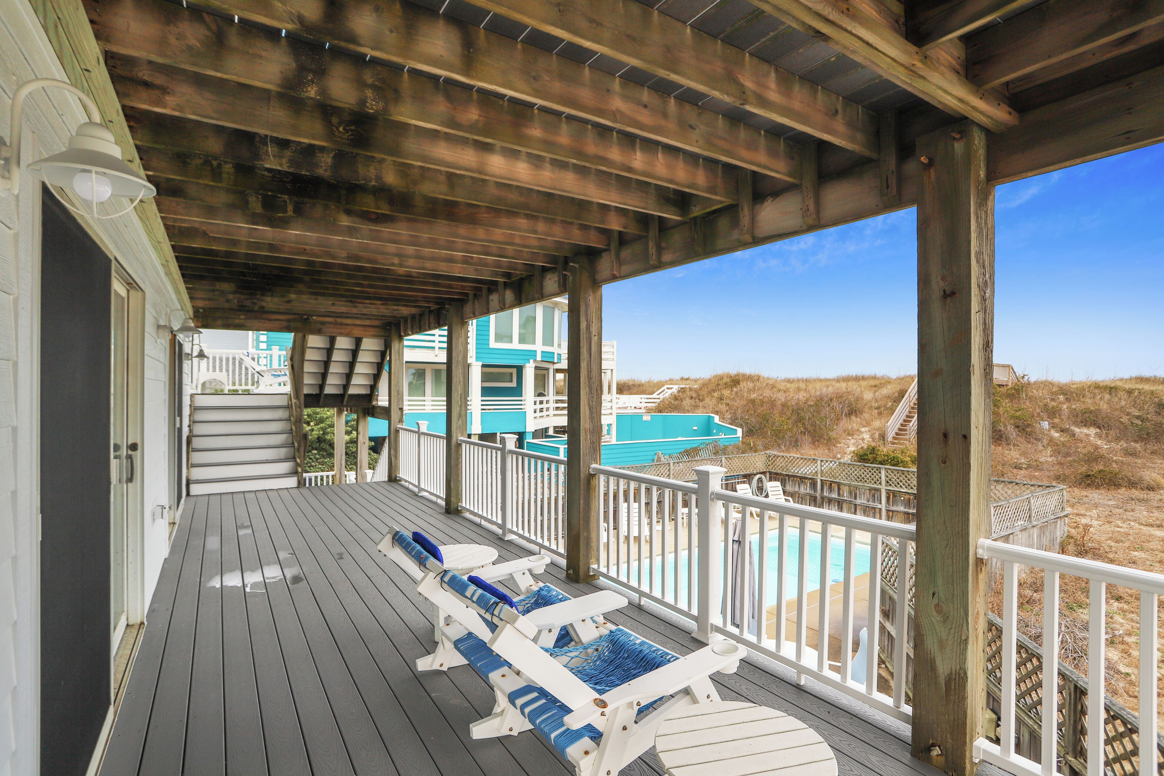 Una terrazza coperta con ringhiere in legno, poltrone relax e vista su una spiaggia e l'oceano.