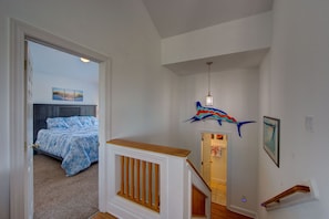 A bedroom with a bed, a wooden bench, a staircase, and a hallway with a decorative fish sculpture.