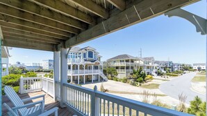 A covered porch with white railings, a wooden deck, and a view of a residential street with houses. - Modern, Community Pool, Quick walk to beach! Hot tub! NH4912 (Nags Head)