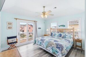 Een slaapkamer met een bed, een plafondventilator, uitzicht door een schuifdeur en een houten stoel.