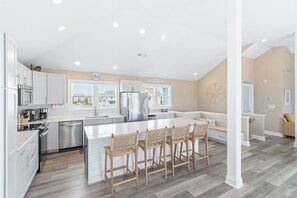 A modern kitchen with white cabinetry, a central island with bar stools, and a view of the beach.