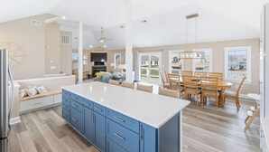 A spacious kitchen with a large island, a dining area with wooden chairs, and a view of the outside. - Modern, Community Pool, Quick walk to beach! Hot tub! NH4912 (Nags Head)