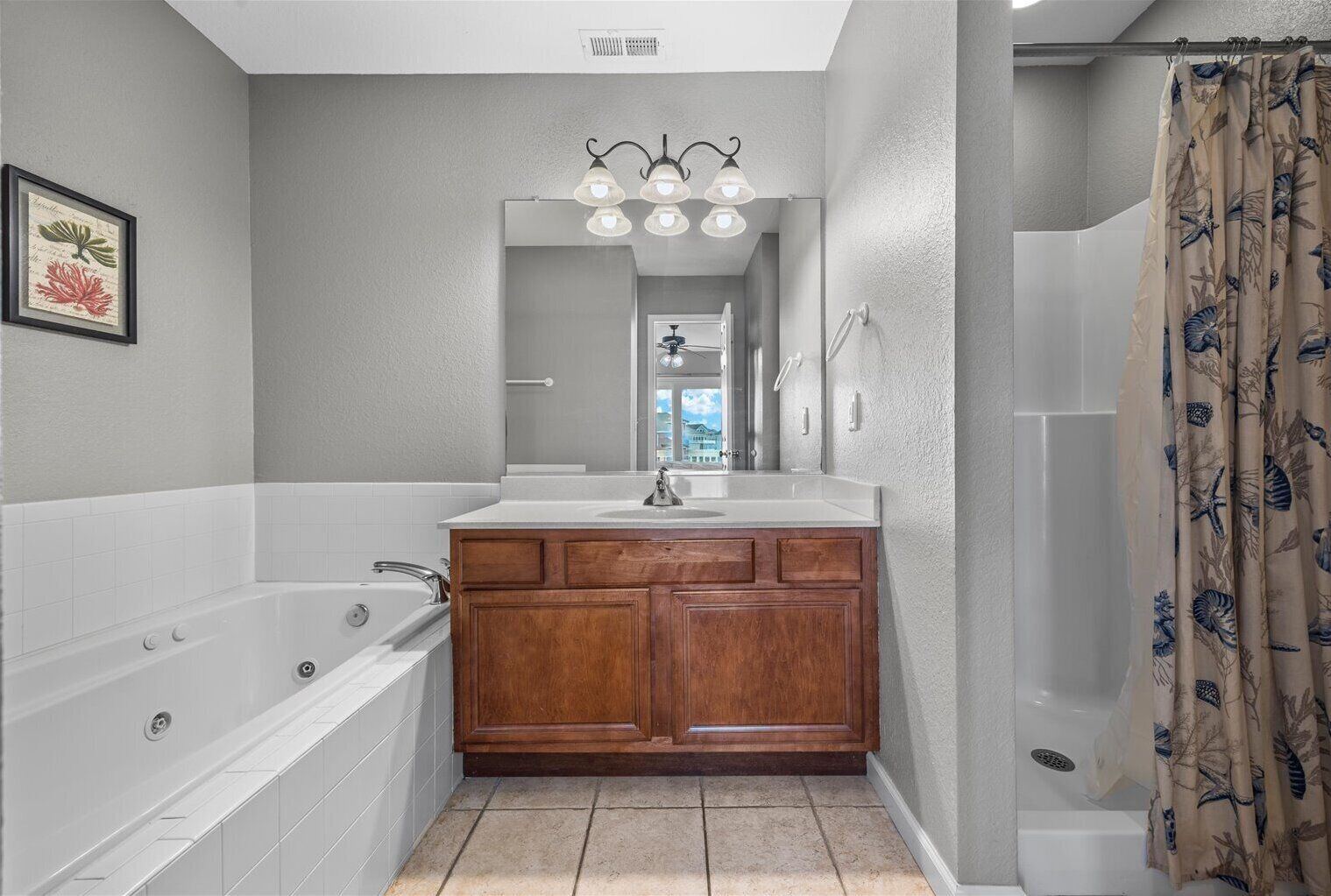 Une salle de bain avec une grande baignoire, un meuble-lavabo en bois, un miroir et un rideau de douche orné d’un motif de feuilles.