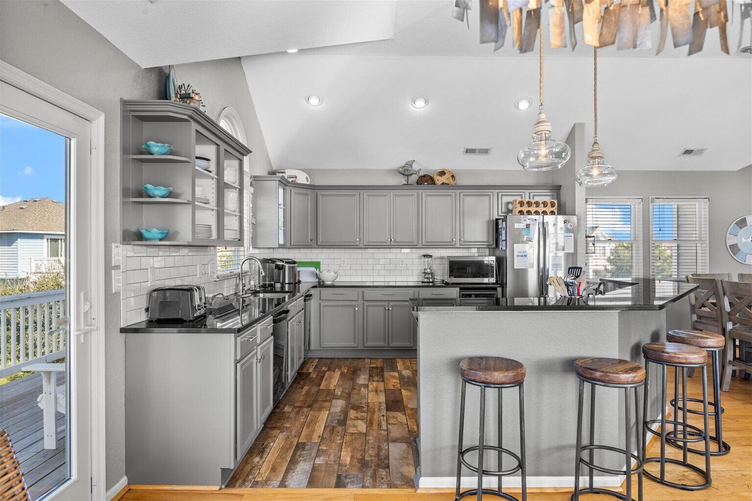 A modern kitchen with grey cabinets, a wooden floor, and a bar area with stools.