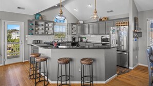 Une cuisine moderne avec des meubles gris, un îlot central doté de tabourets, des appareils en acier inoxydable et des luminaires suspendus.