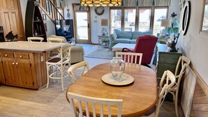 A spacious kitchen with a wooden island, white chairs, and a dining table with a vase. - Steps to the Sand! Ocean Views! Hot tub! Specials! Dogs! KD0223 (Kill Devil Hills)