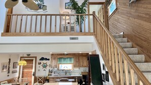A spacious interior with a wooden staircase, a dining area, and a kitchen. - Steps to the Sand! Ocean Views! Hot tub! Specials! Dogs! KD0223 (Kill Devil Hills)