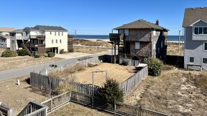 A residential area with houses, a wooden fence, and a beach in the background. - Steps to the Sand! Ocean Views! Hot tub! Specials! Dogs! KD0223 (Kill Devil Hills)