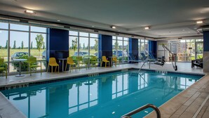 Piscina interior com paredes de vidro transparente, cadeiras amarelas e cadeira de salva-vidas.