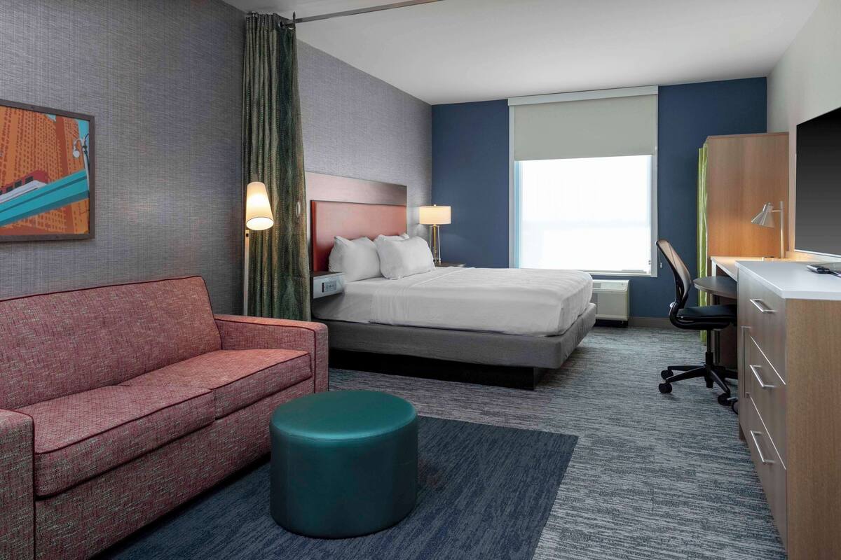 Een hotelkamer met een bed, een bureau, een stoel, een bank en een rond poef.