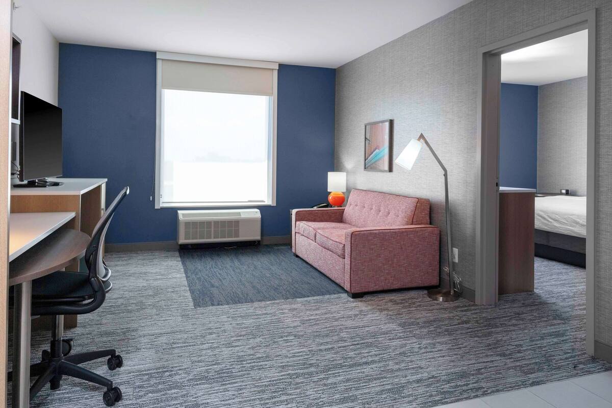Een moderne hotelkamer met een bureau, bureaustoel, een roze bank en een groot raam.