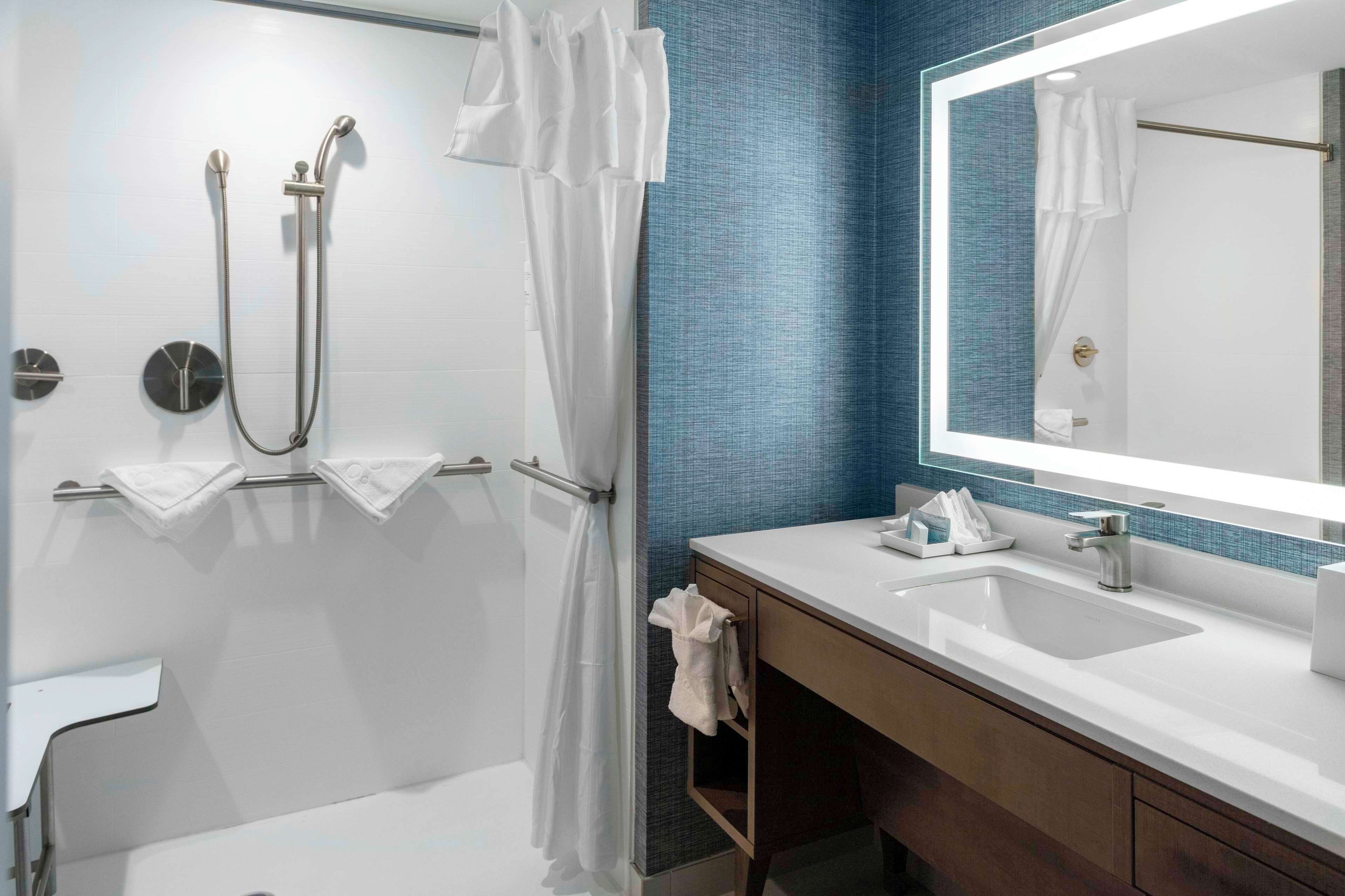 A modern bathroom with a walk-in shower, a large mirror, and a sink with a towel rack.
