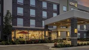 Um hotel moderno com fachada de tijolos, entrada coberta e área externa bem iluminada com mesas e cadeiras.