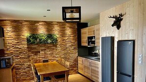 Een moderne keuken met houten kastjes, een eettafel met stoelen, een ingebouwde kruidentuin en een zwarte koelkast.