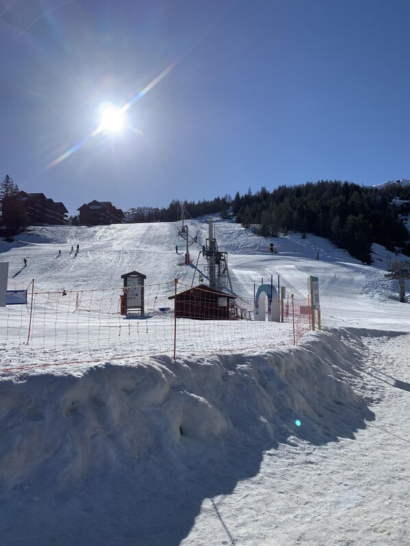 Pista de esquí cubierta de nieve con un telesilla, edificios y un cielo despejado.
