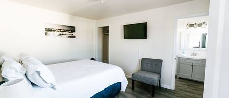 A bedroom with a bed, a chair, a TV, and a view of the bathroom.
