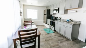 A modern kitchen with white cabinets, a microwave, stove, and a dining area with a table and chairs. - One Block from Ocean CLOSE to everything! Modern and Clean!! (Crescent City)