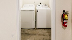 A laundry room with two white washing machines, a fire extinguisher on the wall, and a wooden ceiling beam. - One Block from Ocean CLOSE to everything! Modern and Clean!! (Crescent City)