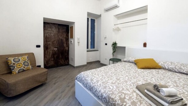 A bedroom with a bed, a sofa, a wooden door, and a small table with towels. - Studios Toledo 355. (Napoli)