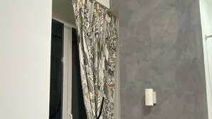 A room with a window, grey textured walls, a white air conditioning unit, and a white wall-mounted light switch. - Studios Toledo 355. (Napoli)