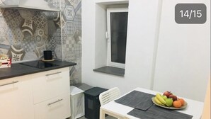 A compact kitchen with white cabinets, a black countertop, a window, and a dining area with a white table and chairs. - Studios Toledo 355. (Napoli)