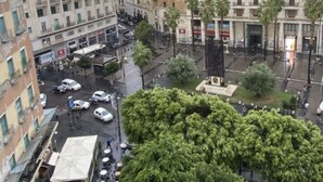 A city street with buildings, parked cars, and a tree-lined square. - Studios Toledo 355. (Napoli)