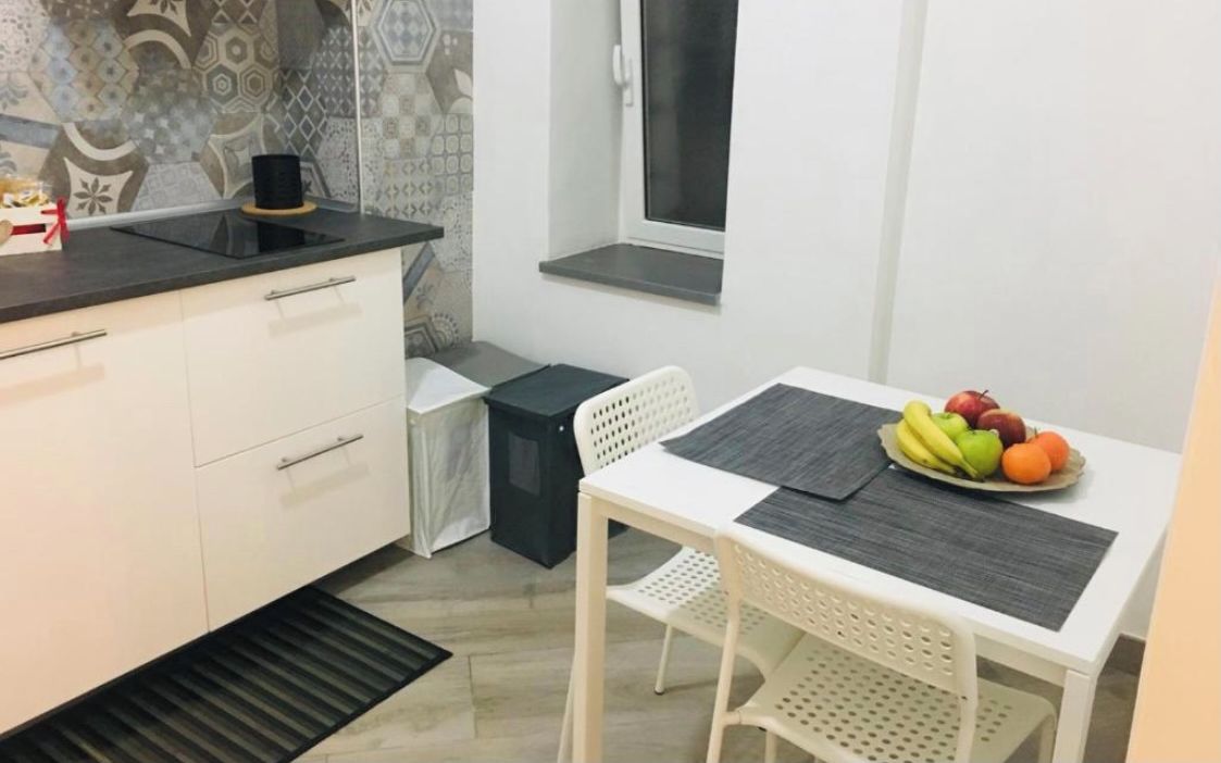 Una cucina compatta con mobili bianchi, un piano di lavoro nero, una finestra e un'area pranzo con tavolo e sedie bianche.