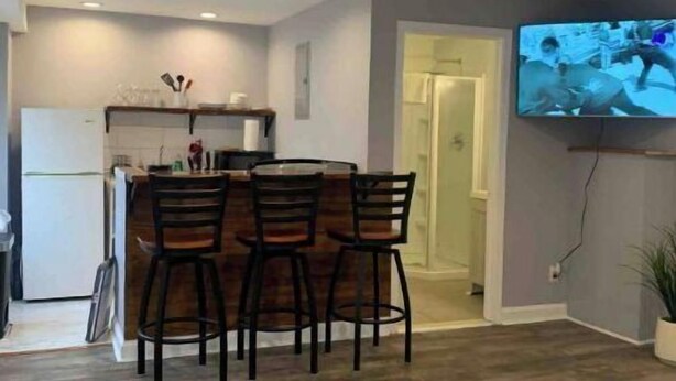 A compact living space with a kitchenette, a dining area with three chairs, a bed, and a TV mounted on the wall. - ✪King Bed Studio✪ in Suburbs -Perfect Long Term Stay (Clifton Heights)